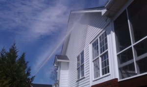 Spraying soft wash solution on white vinyl siding